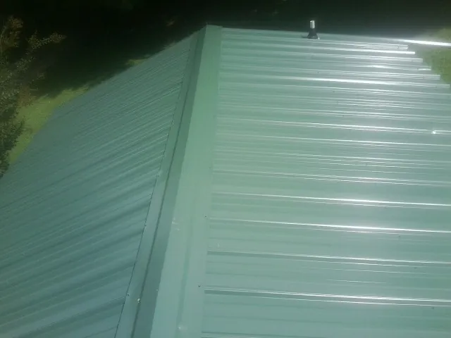 New green metal panels meeting at the ridge of a roof — Flat Roof Repair work by our crew in Celina