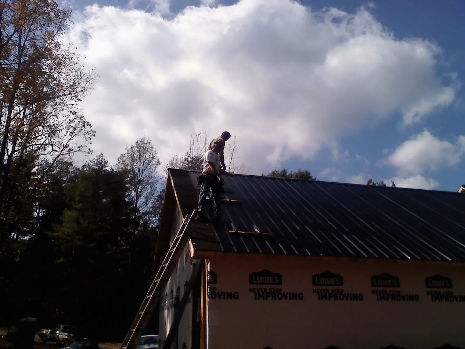 Roofer fastening dark metal panels high against a cloudy sky, from a Roof Inspection job in Celina