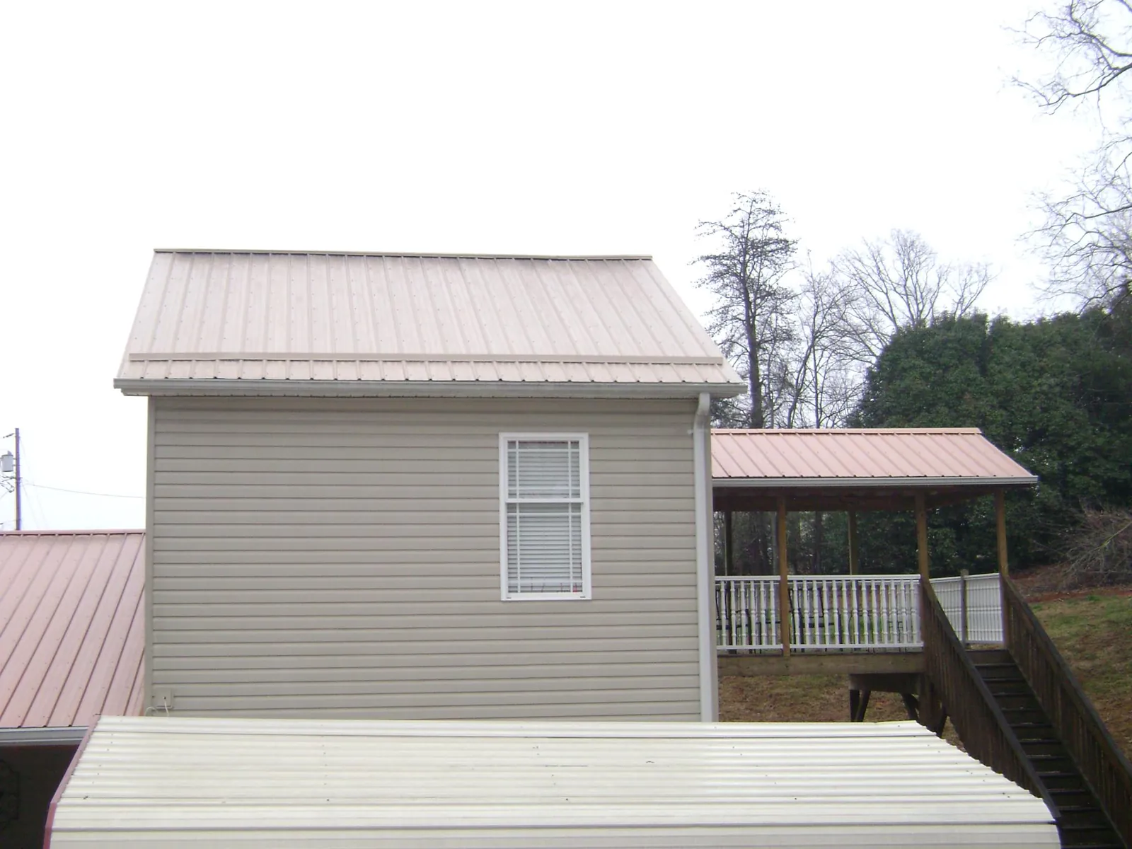 Tan metal roofs on a two story addition and attached porch, from a Roof Replacement job in Celina